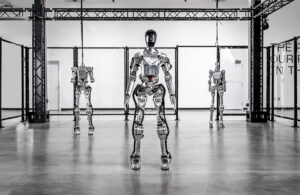 A figure 01 humanoid robot stands upright with two partial (headless) torsos suspended on each side.